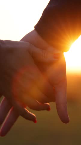 Close-up of the silhouettes of a couple in love holding their hands together and the golden sun gently setting below the horizon. The man and woman have their hands clasped tightly, romantic scene at sunset, slow motion. Couple stands close together deep bond and emotional connection.