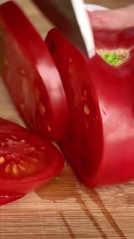 Close-up of a chef slicing a red juicy tomato with a knife on a wooden board