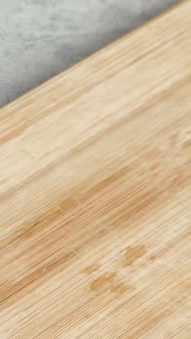 Woman's hand using a sharp knife for slicing a fresh, ripe green cucumber on a wooden cutting board. Healthy food preparation for a salad