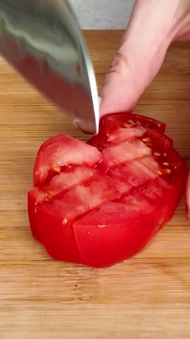 Detailed view of a chef's hands chopping a juicy red tomato with a sharp kitchen knife on a bamboo cutting board for a healthy salad
