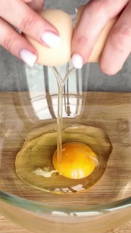 Woman's hands breaking a fresh egg with a knife into a glass bowl