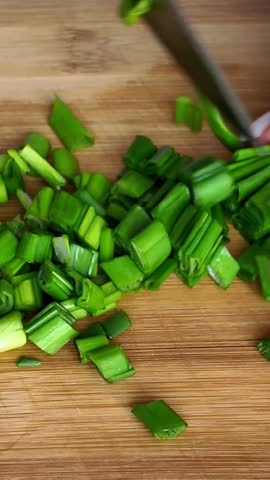 Woman's hands slicing fresh green onions on wooden board
