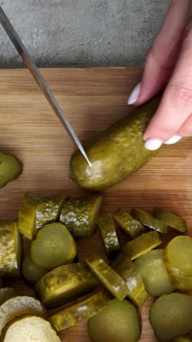 Woman's hands slicing pickled cucumber on wooden board