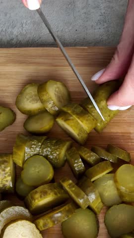 Woman's hands slicing pickled cucumber on wooden board