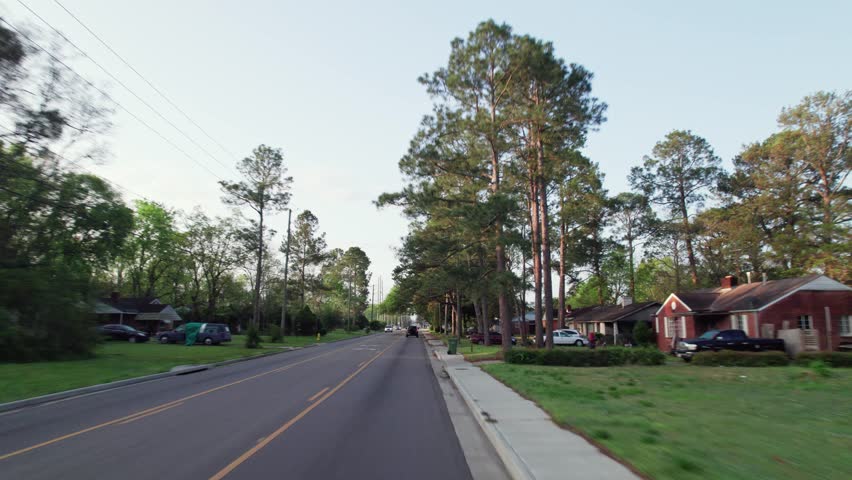 Moving past middle lower class poor neighborhood street homes outside downtown capital city Montgomery, Alabama in historic suburb community with houses, buildings, sidewalk, cars, driveways, and road