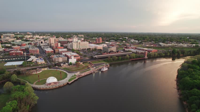 Aerial drone landscape view of downtown Montgomery, Alabama riverfront water park along gun island shoot river with baseball ballpark stadium, green lawn, buildings, high-rises, and capital city roads