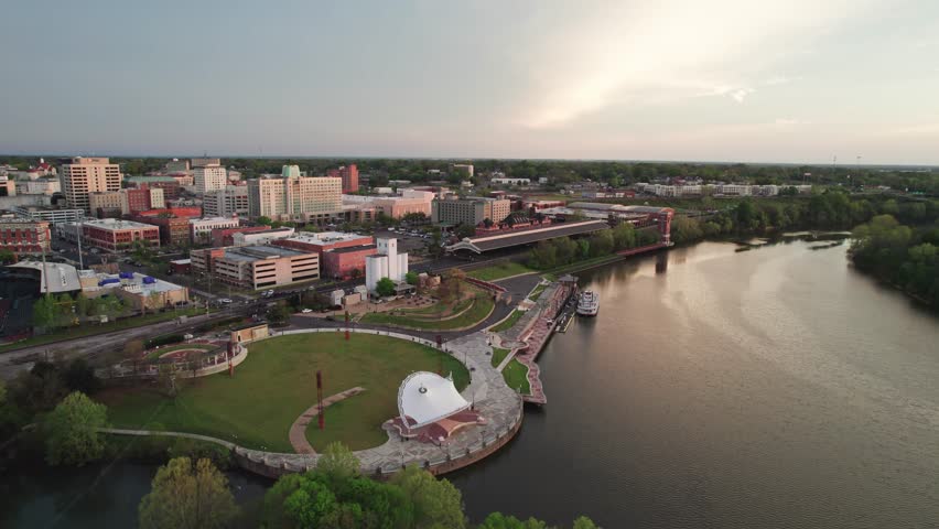Aerial drone landscape view of downtown Montgomery, Alabama riverfront water park along gun island shoot river with baseball ballpark stadium, green lawn, buildings, high-rises, and capital city roads