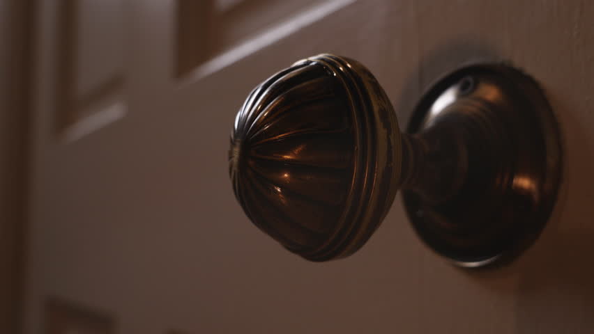 A detailed view of an ornate brass door knob on a wooden door. Moving door handle. The lighting highlights the intricate design of the knob.