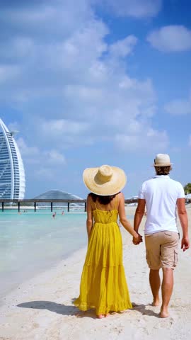 Rear view of a happy couple on summer vacations walking down a beautiful beach in Dubai, UAE