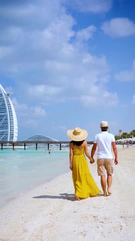 Rear view of a happy couple on summer vacations walking down a beautiful beach in Dubai, UAE