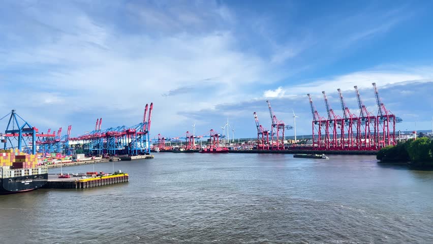 Hamburg, Germany. May 24, 2024. Large cranes move containers at busy port during sunny afternoon hours near waterway