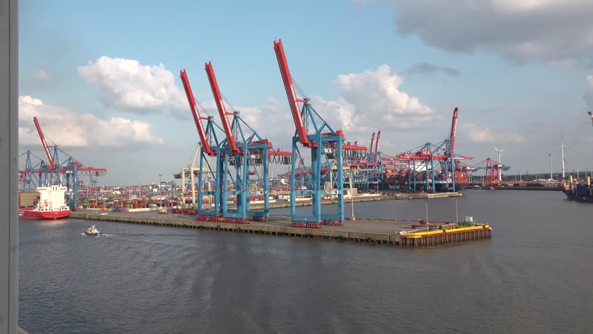 Hamburg, Germany. May 24, 2024. Large cranes move containers at busy port during sunny afternoon hours near waterway