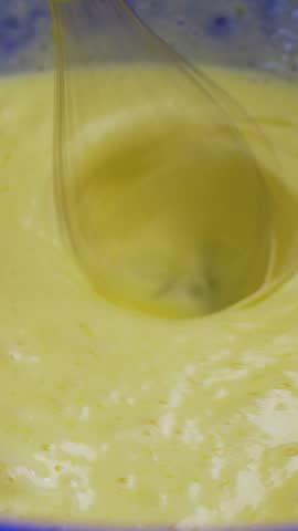 Female cook in home kitchen uses hand mixer. Blue bowl holds egg liquid dough. Whisk ensures even blend before pancake cooking