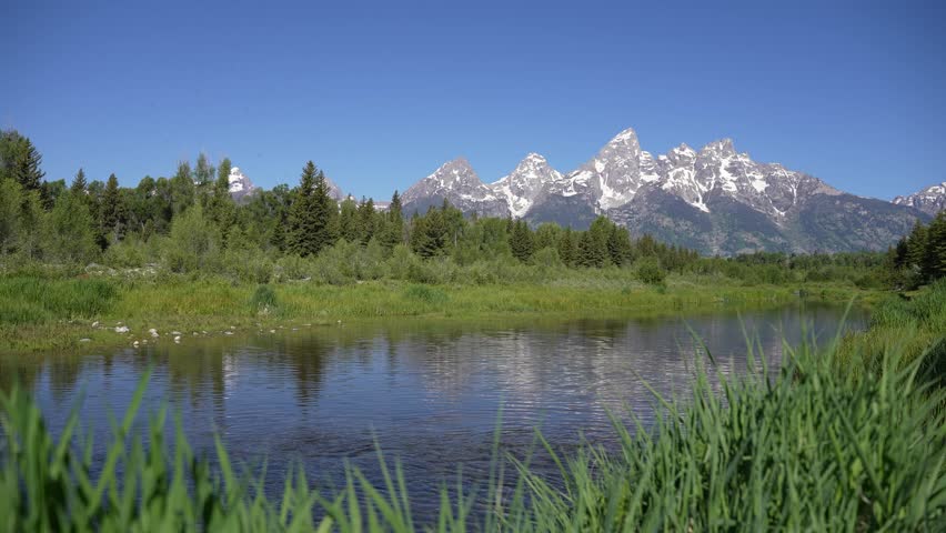 A river flowing in front of the Grand Teton Mountains in Grand Teton National Park, Wyoming. Scenic alpine landscape highlighting moving water, majestic mountain peaks, and serene natural surroundings.