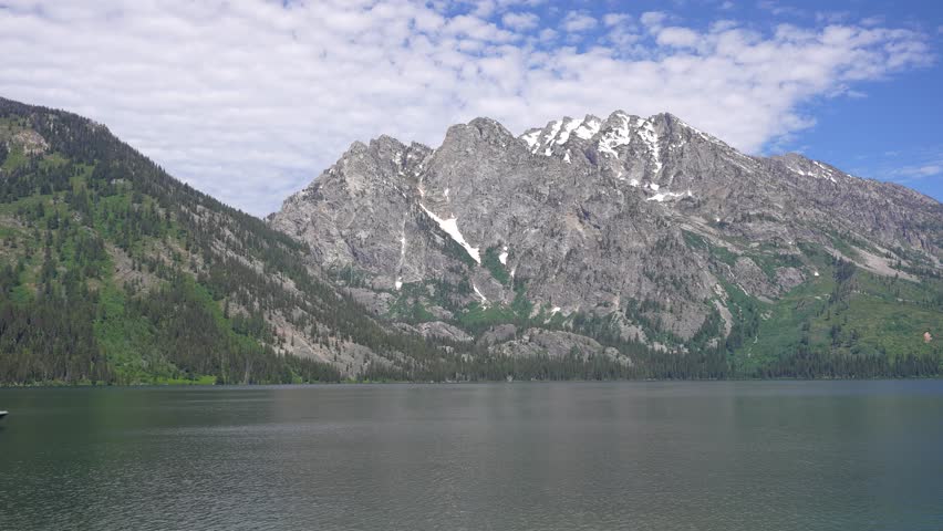 Wide shot of Jenny Lake in Grand Teton National Park, Wyoming, as a tour boat slowly enters the frame. Scenic alpine landscape featuring calm waters, towering mountain peaks, and a peaceful natural atmosphere.