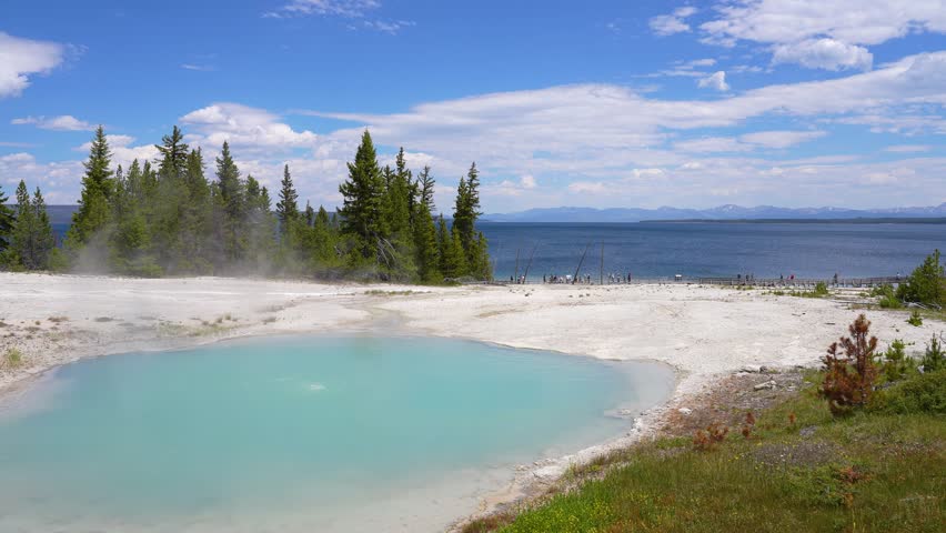 Close-up shot of vivid blue geothermal water formed by a geyser with Yellowstone Lake visible in the background at Yellowstone National Park, Wyoming.