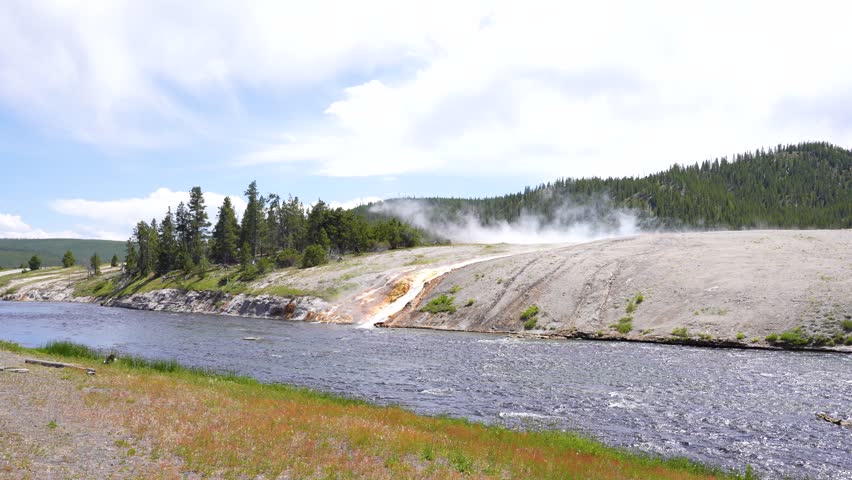 Shot of a geyser flowing and mixing with a river at Yellowstone National Park, Wyoming. Stunning geothermal scenery capturing the interaction of hot springs with flowing water in a dramatic natural landscape.