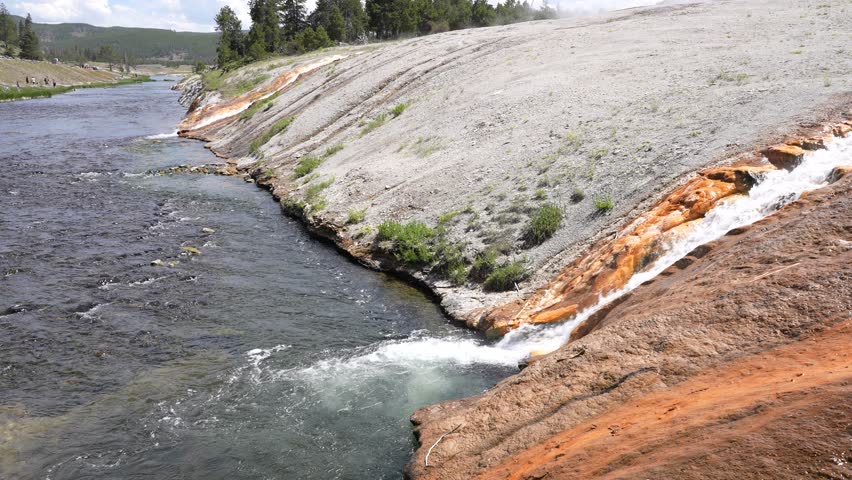 Close-up shot of a geyser mixing with a river at Yellowstone National Park, Wyoming. Detailed view capturing the interaction of steaming hot spring water with the flowing river in a dramatic and scenic natural landscape.