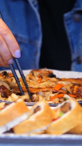 Closeup of a young woman wearing a denim jacket enjoying a traditional asian meal, picking up stir fried udon noodles with chopsticks from a plate in a japanese restaurant