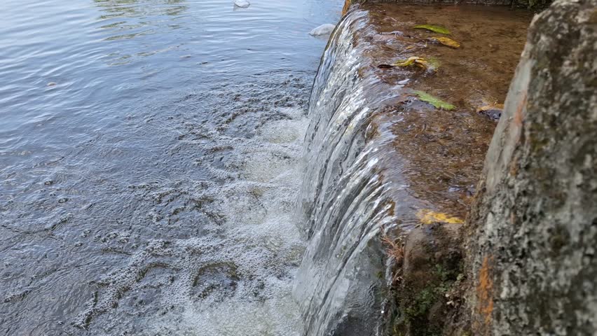 Close Up of Water Flowing Like a Mini Waterfall in a Concrete Gutter, Clear Stream Cascading Over Stone Ledge, Urban Drainage System and Environmental Water Flow