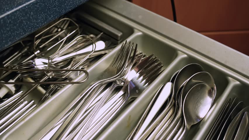 Close-up of organized stainless steel silverware in a cutlery tray—forks, knives and spoons neatly stacked in a drawer, clean kitchen storage and tableware organization.