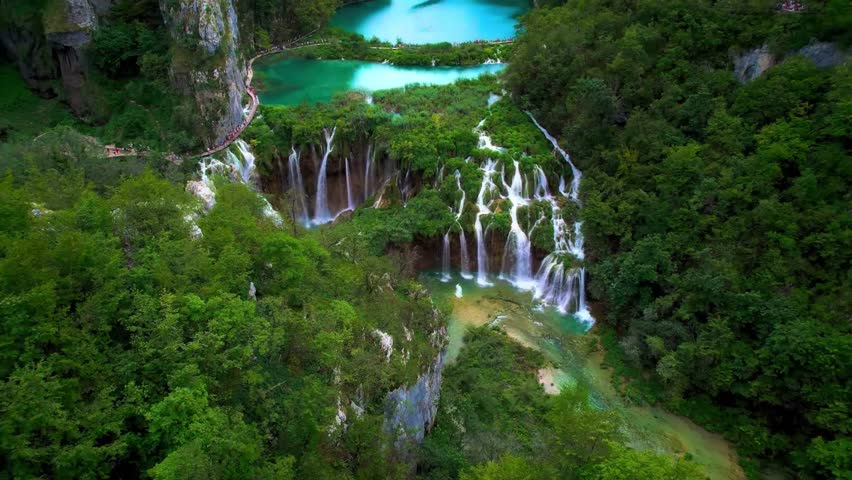 An aerial view captures the stunning natural beauty of a national park with numerous waterfalls and vibrant blue lakes surrounded by dense forest foliage