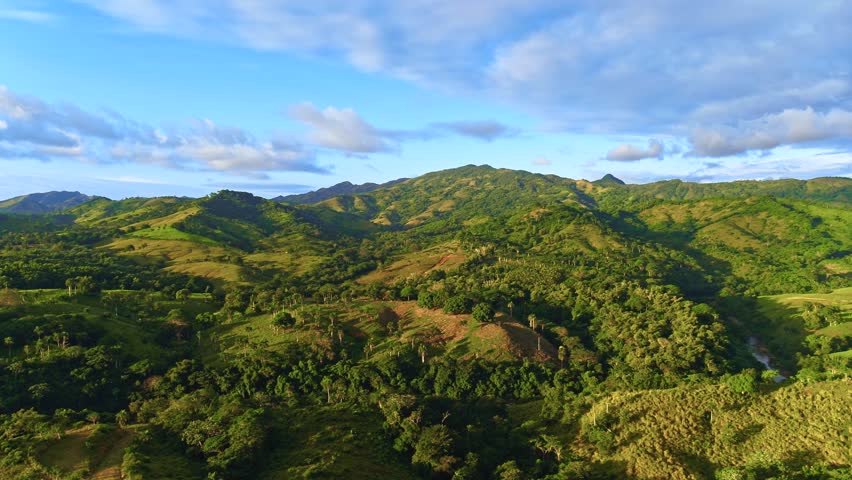 Aerial landscape of a mountain range in the clouds. Grassy fields and hills in the evening light. Cloudy sky over mountain peaks. Summer in the Dominican Highlands. Beautiful summer landscape in the mountains.
