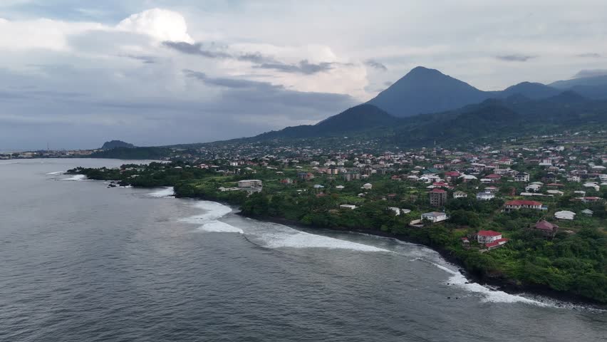 A high-angle drone perspective of the coastal city of Limbe, Cameroon, with the majestic Mount Cameroon rising in the misty background