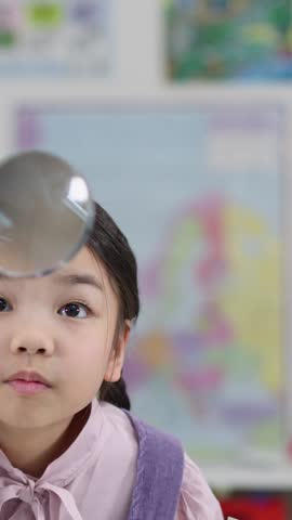 A young girl with braided hair investigates closely using a magnifying glass in class.