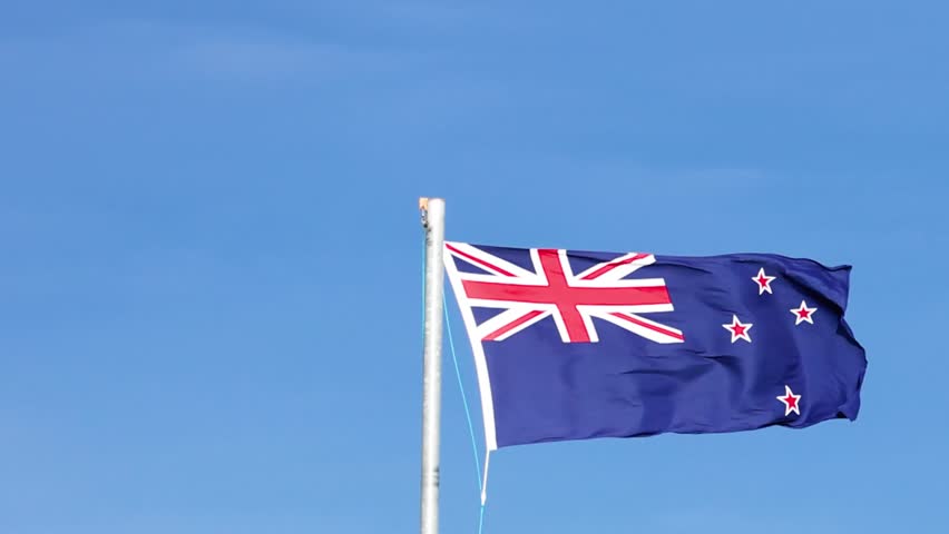 The New Zealand flag flutters vigorously on a silver flagpole under bright daylight conditions.