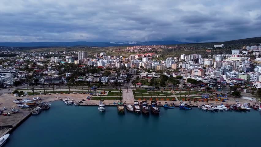 Quaint coastal cityscape with bustling harbor filled with boats. Overcast sky adds dramatic effect as sunset illuminates the vibrant urban life surrounding the shoreline.
