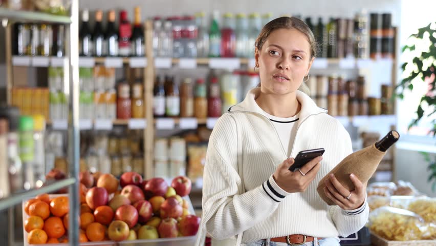 Young woman scans a bottle of Spanish wine using a barcode. Supermarket visitor pays for purchases online using an application and a QR code. High quality 4k footage