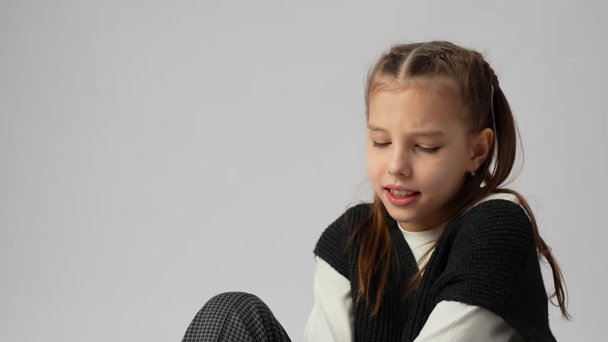 Cheerful young girl with a wide, genuine smile and squinted eyes, expressing pure happiness and laughter. Studio portrait on a grey background