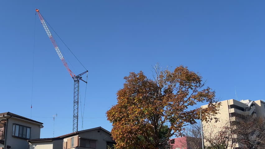 Tall construction crane turns against blue sky, low angle building site