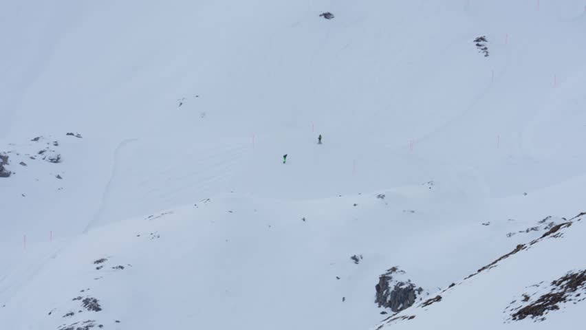 Two professional skiers descending a steep, off piste slope in the vast, snowy mountains