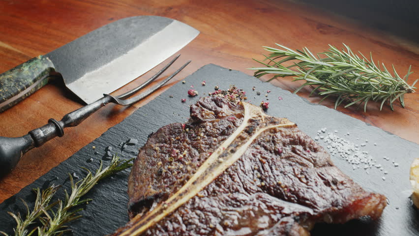 T-bone steak with herbs and garlic on the serving slate board close-up. Top view.