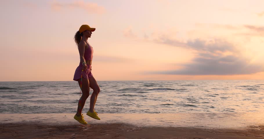 Fit young woman jumping rope at the beach. Sportswoman against sea and sky background. Summer sport and healthy lifestyle concept. Slow motion