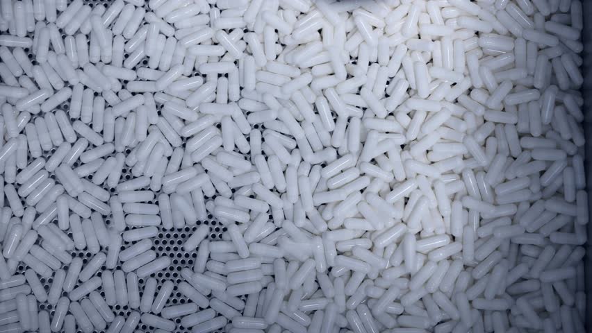 Manufacturing process, white capsules moving on conveyor in modern pharmaceutical factory. Medical production line.