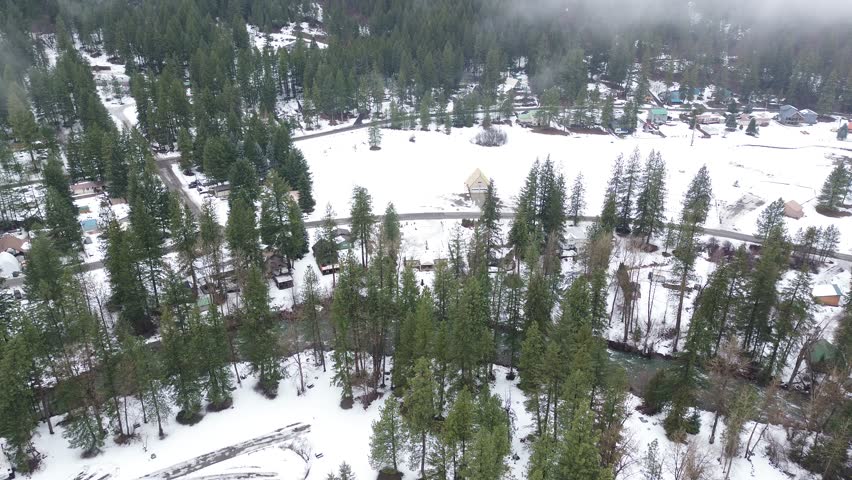 Open snowfield near Peshastin Creek sits between wooded residential pockets, winding local roads west of Blu Shastin RV Park. Frosted roofs, dense evergreens, diffused winter light Peshastin, WA. USA