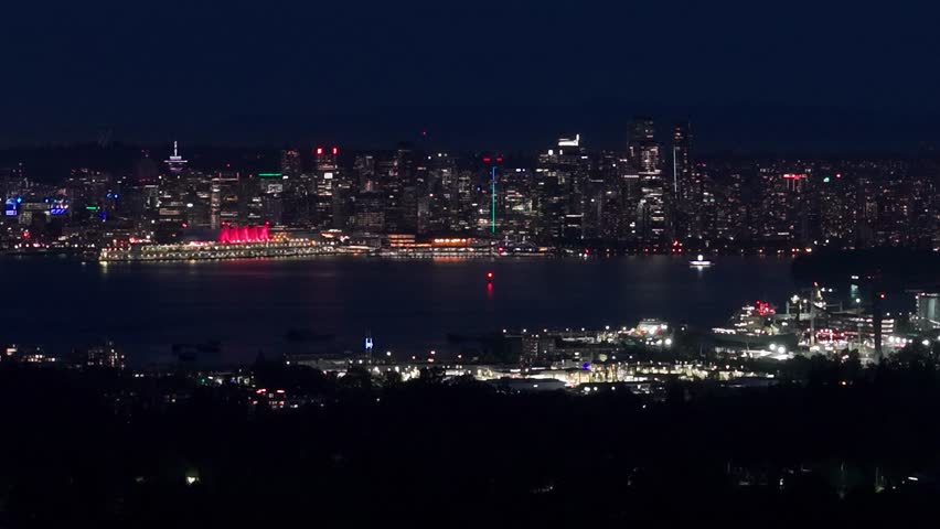 Nighttime panoramic view of Vancouver’s downtown skyline seen across Vancouver Harbour, featuring illuminated skyscrapers, glowing waterfront lights, and reflections on calm water under a dark sky.