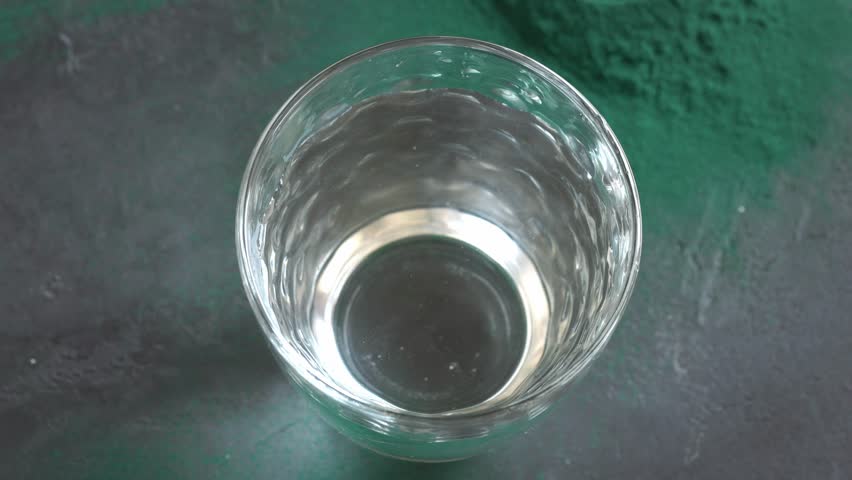 Putting a scoop of green spirulina algae powder into a glass of water, top view