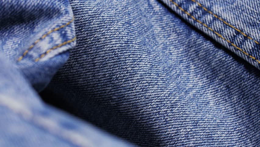 Macro pan across blue denim jeans fabric with seam stitching in frame