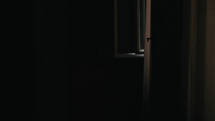 In the dark bedroom, the window is open and the curtains flutter. A calm, quiet stillness reigns in the room. The curtains flutter gently in the wind.