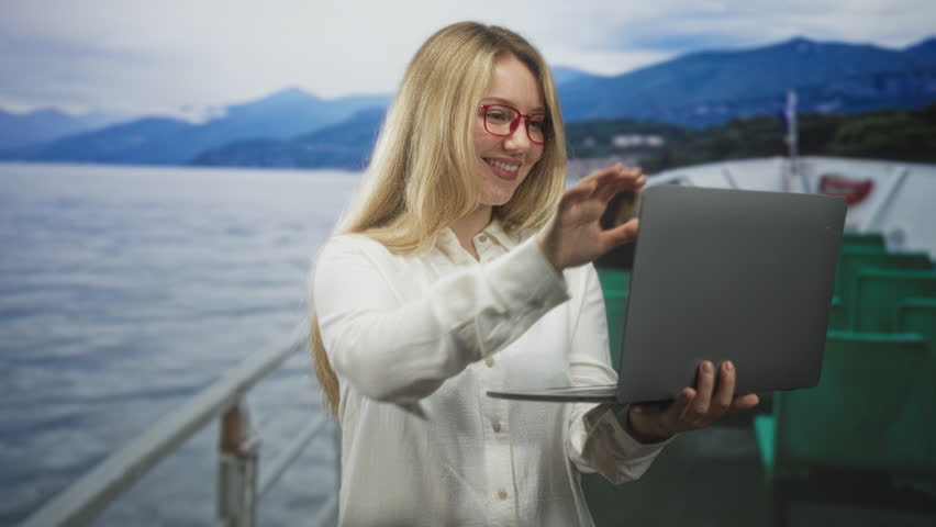 Woman hugging laptop on ferry deck street, smiling with red glasses and bare hands holding computer close; travel joy.
