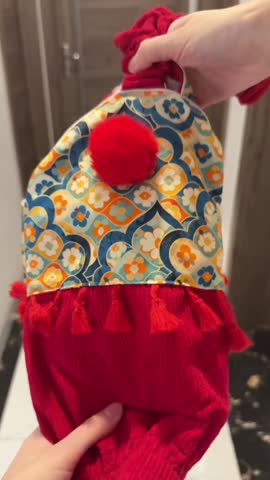 Adorable golden retriever dog wearing a detailed traditional chinese style costume featuring bright red fabric and a semicircular bib with vibrant blue orange and white floral patterning stands happily indoors ready for celebration.