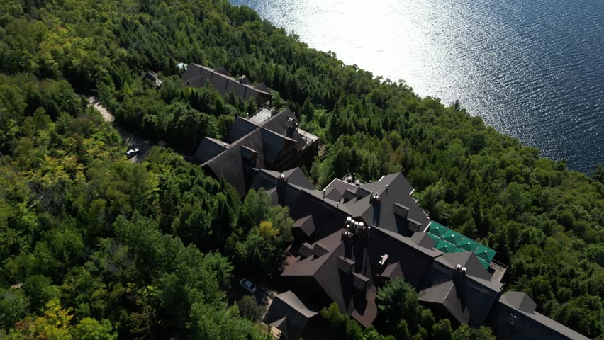 Aerial pullback from Hotel Sacacomie rooftop buildings nestled within forest beside the lake