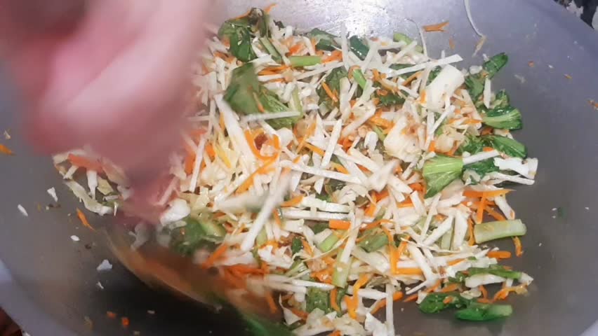 Fresh vegetables such as carrot, cabbage, and spring onion being stir-fried in frying pan. Healthy homemade meal preparation, Asian cooking, and simple kitchen lifestyle concept