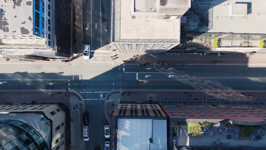 Top view, cyclists glide through busy downtown Halifax. Roads lined with tall buildings, streetlights, and cars show the vibrant city atmosphere in sunny Nova Scotia.Urban Cycling Group Biking Through