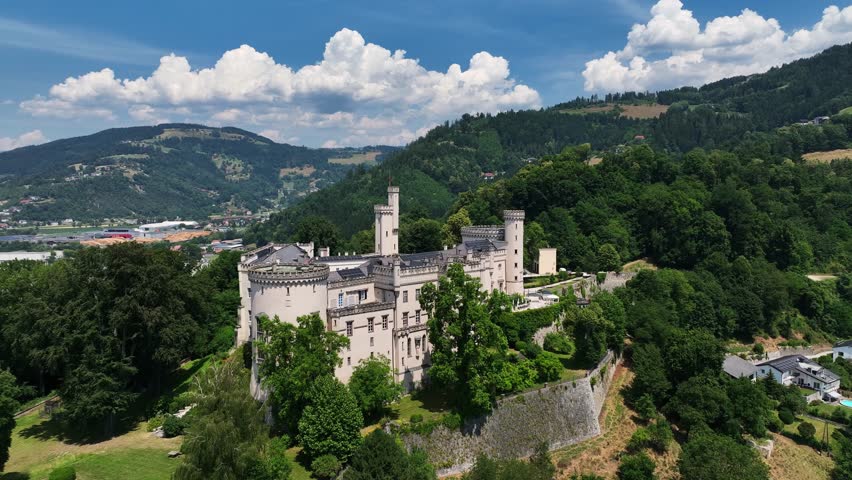 Aerial summer footage of Wolfsberg showing town center, church towers, green hills, layered valleys, warm light, smooth drone flight, atmospheric European small-town scenery