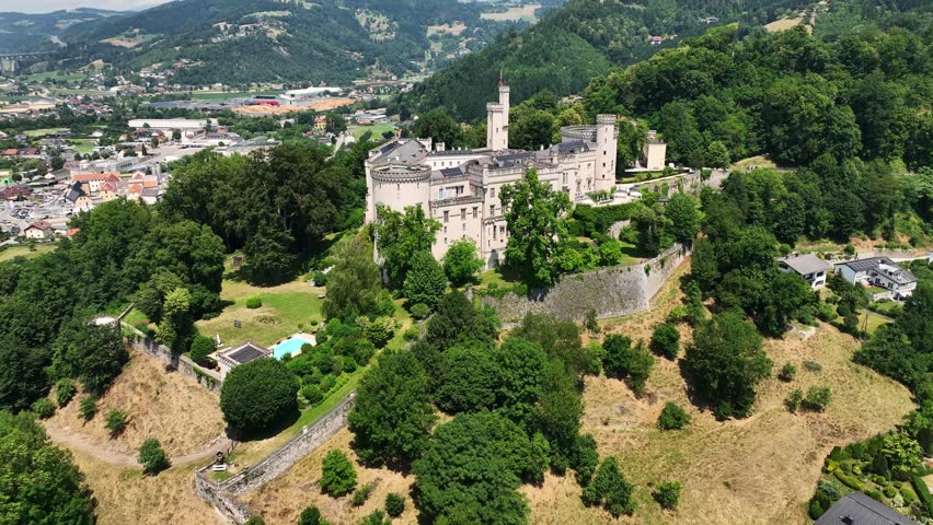 Aerial summer footage of Wolfsberg showing town center, church towers, green hills, layered valleys, warm light, smooth drone flight, atmospheric European small-town scenery